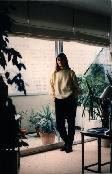 Jeune femme souriante debout près d'une baie vitrée avec des plantes.ᴬᴵ