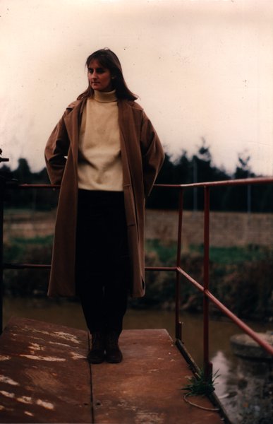 Femme en manteau beige appuyée à une rambarde métallique au bord d'un canal.ᴬᴵ