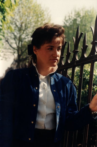 Femme en veste bleue tenant une grille en fer forgé, regard de côté.ᴬᴵ