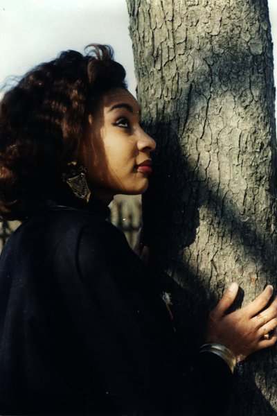 Femme aux cheveux bouclés appuyant son visage contre un tronc d'arbre.ᴬᴵ