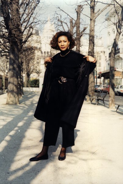 Femme ouvrant son manteau noir, posant dans une rue de Paris.ᴬᴵ