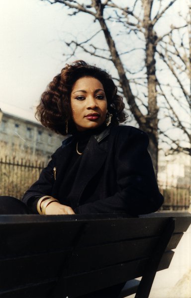 Femme aux cheveux bouclés assise sur un banc, regard de côté.ᴬᴵ