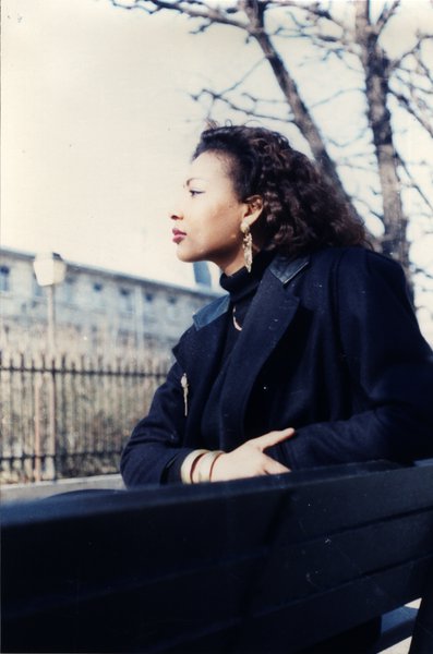 Femme aux cheveux bouclés assise sur un banc, vue de profil.ᴬᴵ