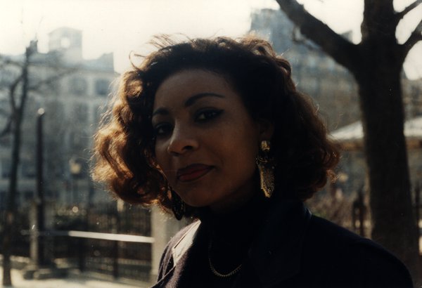 Portrait souriant d'une femme aux cheveux bouclés, immeubles en arrière-plan.ᴬᴵ