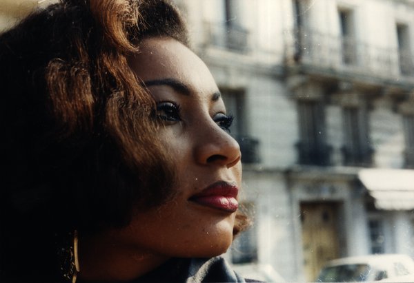 Portrait de profil d'une femme aux cheveux bouclés, façade d'immeuble en arrière-plan.ᴬᴵ
