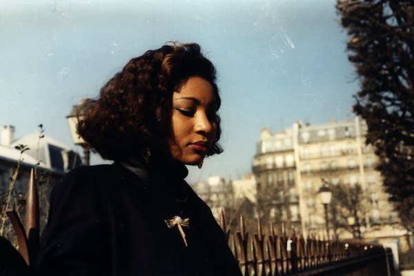 Femme aux cheveux bouclés avec une broche libellule, immeubles en arrière-plan.ᴬᴵ