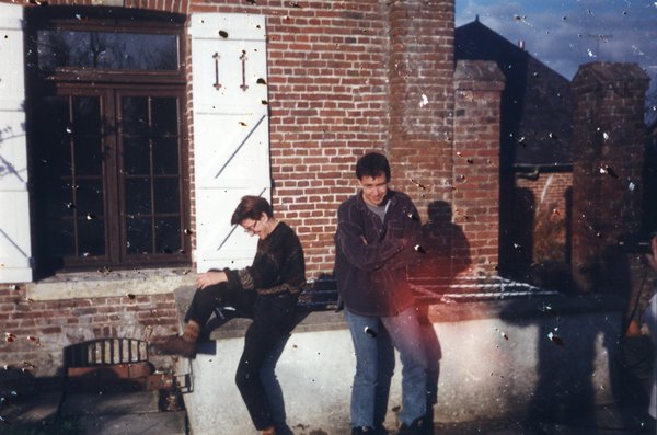 Homme et femme riant sur un parapet devant une maison en briques.