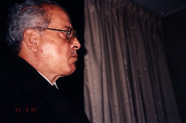 Homme âgé de profil avec des lunettes devant un rideau.ᴬᴵ