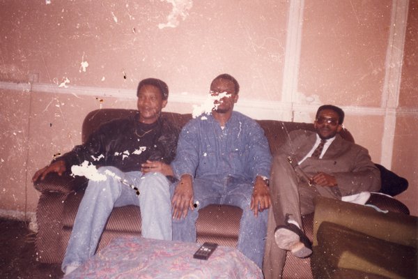 Trois hommes assis sur un canapé brun.