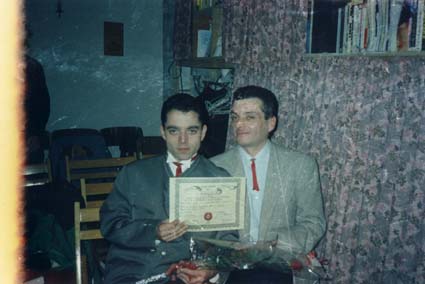 Deux hommes en complet et lavallières rouges assis côte à côte, un diplôme dans les mains.