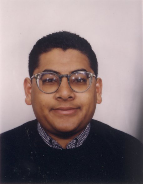 Visage d’homme brun à lunettes souriant.