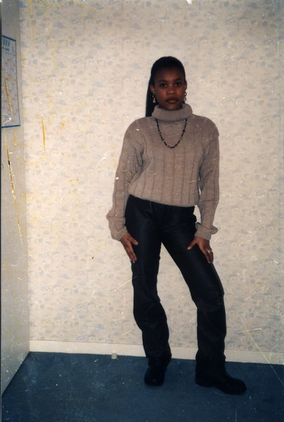 Jeune fille pose en pull et pantalon devant un mur. `