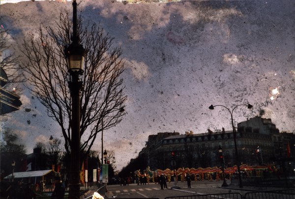 Boulevard parisien avec arbres, lampadaire, manifestants en arrière-plan.