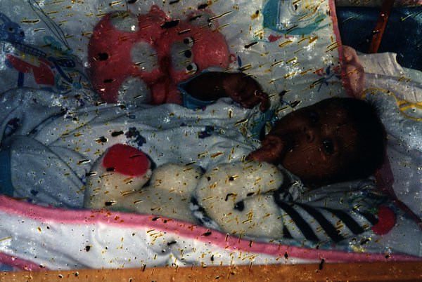 Bébé dans un berceau avec une peluche. Image avec taches.ᴬᴵ