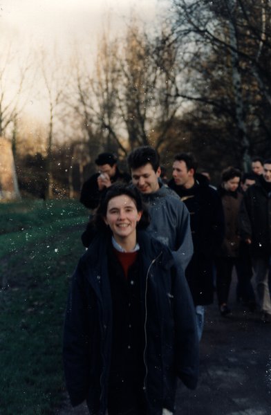 Femme souriante marchant dans un parc, groupe à l'arrière-plan.ᴬᴵ