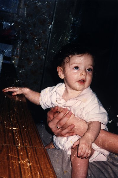Bébé tenu sur les genoux de quelqu'un près d'une table en bois.ᴬᴵ
