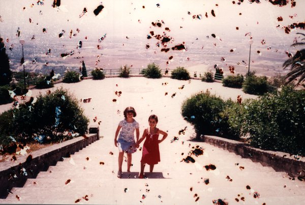 Deux fillettes sur une terrasse surplombant un paysage. Image avec de nombreuses taches.ᴬᴵ