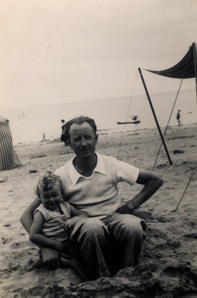Homme tenant un enfant sur une plage, bateau et tente en arrière-plan. Noir et blanc.ᴬᴵ