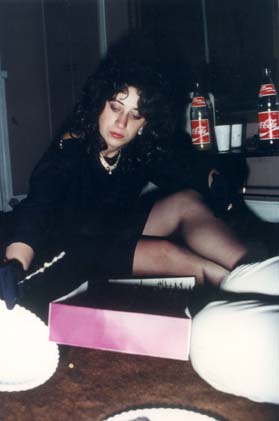 Jeune femme brune en collant noir assise sur un sol en moquette ouvre une boîte à gâteau.