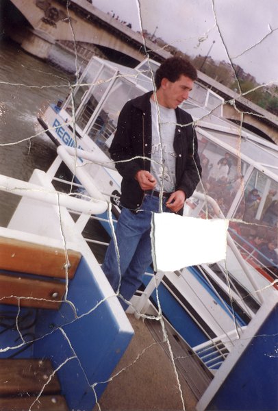 Homme brun accoudé au bastingage d’un bateau-mouche. Image déchirée en partie reconstituée.