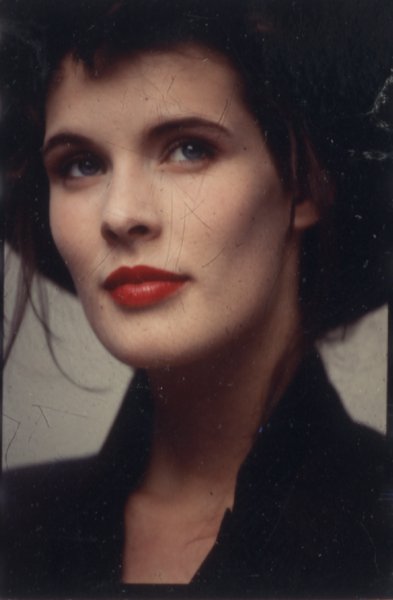 Visage de femme brune aux yeux bleus, les lèvres peintes en rouge.
