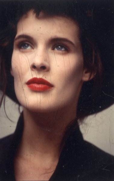 Visage de femme brune aux yeux bleus, les lèvres peintes en rouge.