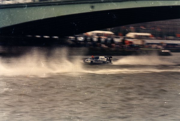 Bateau de course passant sous un pont, spectateurs sur les rives.ᴬᴵ