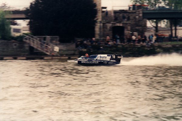 Bateau de course Boutté numéro 10 devant une tour en pierre et une foule de spectateurs.ᴬᴵ