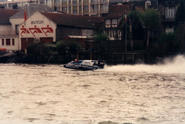 Bateau de course Boutté numéro 10 devant un club d'aviron et une maison à colombages.ᴬᴵ