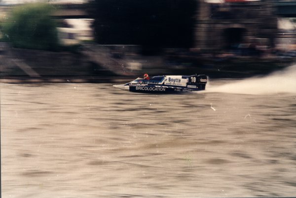 Bateau de course Boutté numéro 10 longeant un mur de pierre avec spectateurs.ᴬᴵ