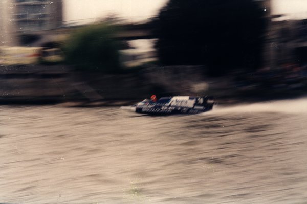 Bateau de course longeant une rive arborée, effet de mouvement.ᴬᴵ