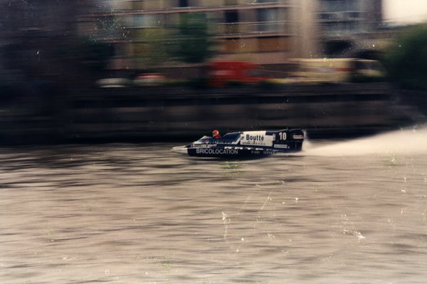 Bateau de course Boutté numéro 10 devant des immeubles, effet de mouvement.ᴬᴵ