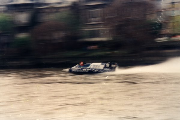 Bateau de course devant des maisons à toits de tuiles rouges, effet de mouvement.ᴬᴵ
