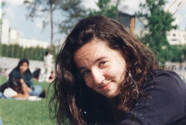 Visage de jeune fille brune de trois quarts, pelouse en arrière-plan.