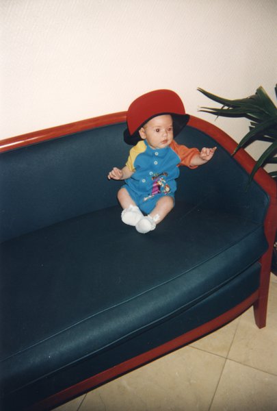 Bébé assis sur un divan bleu avec une casquette sur la tête.