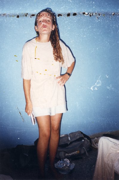 Adolescente à longs cheveux blonds en mini-robe blanche, une brosse à cheveux dans la main, debout devant un mur bleu.