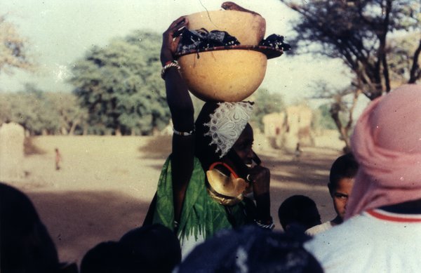 Femme en habit traditionnel avec des calebasses posées sur la tête.