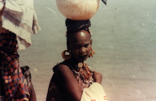 Jeune fille en habit traditionnel et bijoux avec sur le haut de la tête une calebasse.